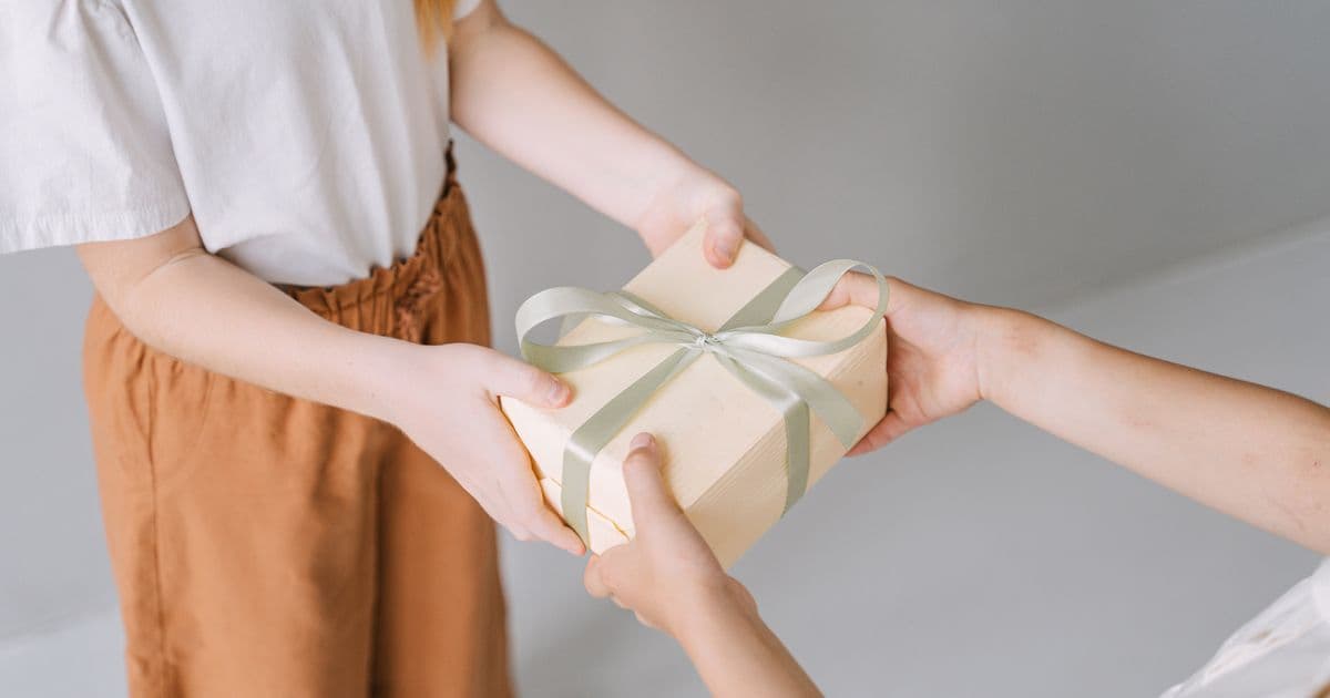 Two pairs of hands exchanging a ribbon-tied gift box