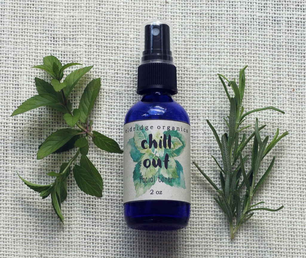 A Chill Out facial toner bottle next to fresh mint and rosemary sprigs