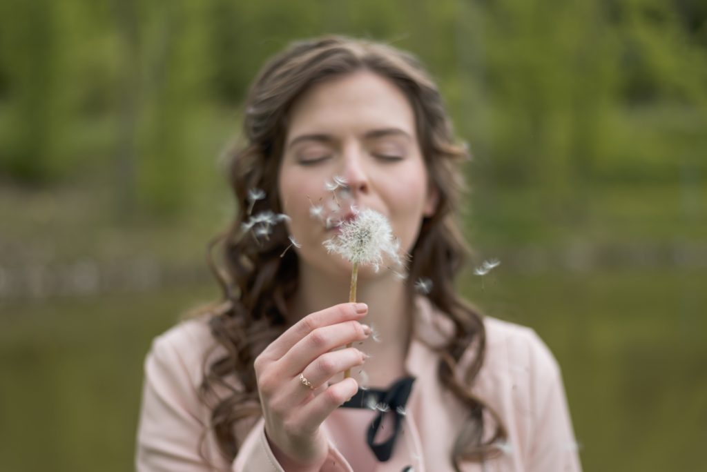 Woman in a pink coat blowing the seeds off a dandelion outdoors