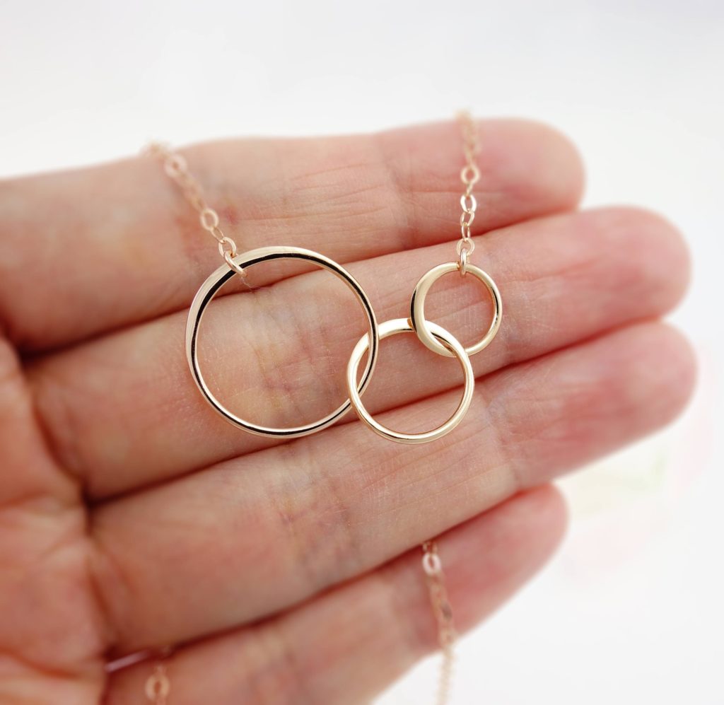 Rose-gold necklace with three interlaced circles held in the palm of a hand