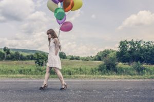 Woman in a white dress walking down a country road holding a bunch of colorful balloons