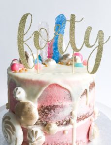 Gold glitter cake topper reading forty on a drip cake decorated with pastel candy