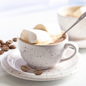 Cup of coffee topped with melted marshmallow and coffee beans on the saucer