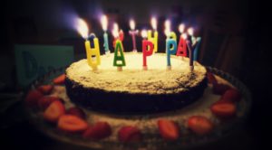 Chocolate birthday cake topped with colorful lit Happy Birthday candles and strawberries