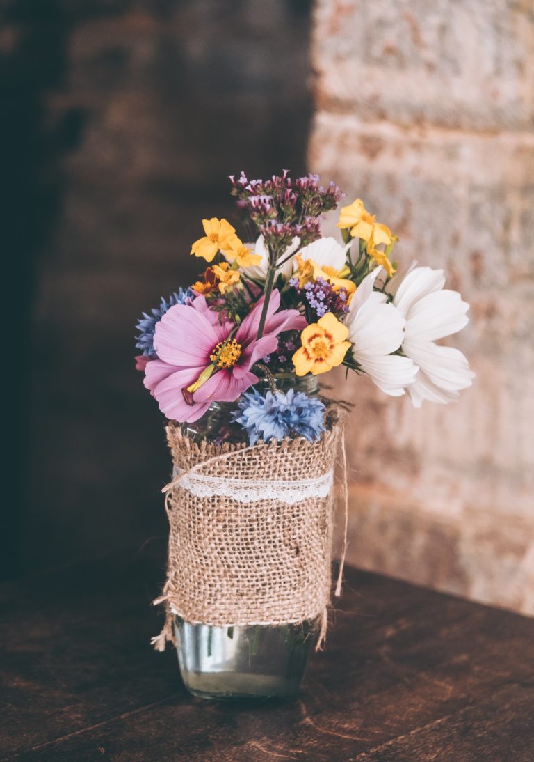 A rustic bouquet of wildflowers wrapped in burlap and lace, set on a wooden table