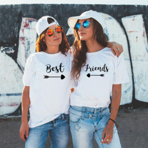 Two friends wearing matching white Best Friends t-shirts with an arrow and heart design