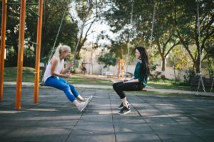 Two friends sitting on park swings facing each other and talking