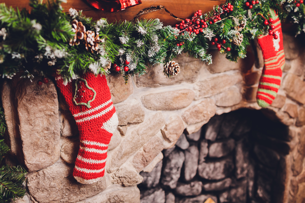 Row of red knit Christmas stockings hanging from a garland-covered stone fireplace mantel