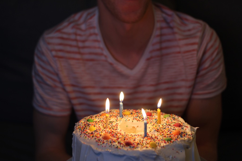A man blowing out candles on a sprinkle-covered birthday cake