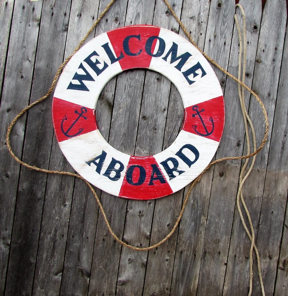 A red-and-white wooden life preserver sign reading 'Welcome Aboard' with anchor details