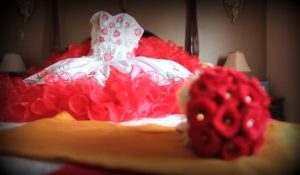 Red and white ruffled Quinceanera dress laid out on a bed next to a red rose bouquet