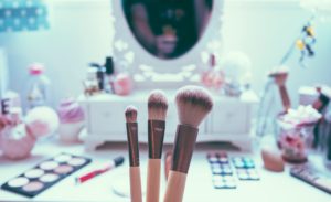 Makeup brushes standing on a vanity table surrounded by cosmetics, with a mirror in the background