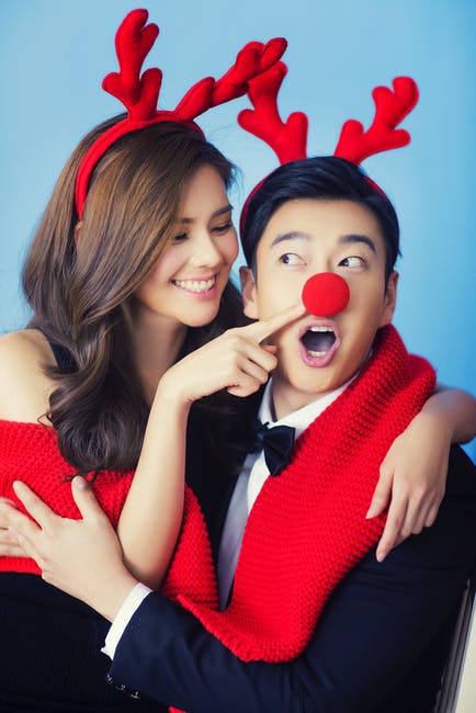 Couple wearing reindeer antler headbands and a red clown nose, one pointing playfully at the other's nose