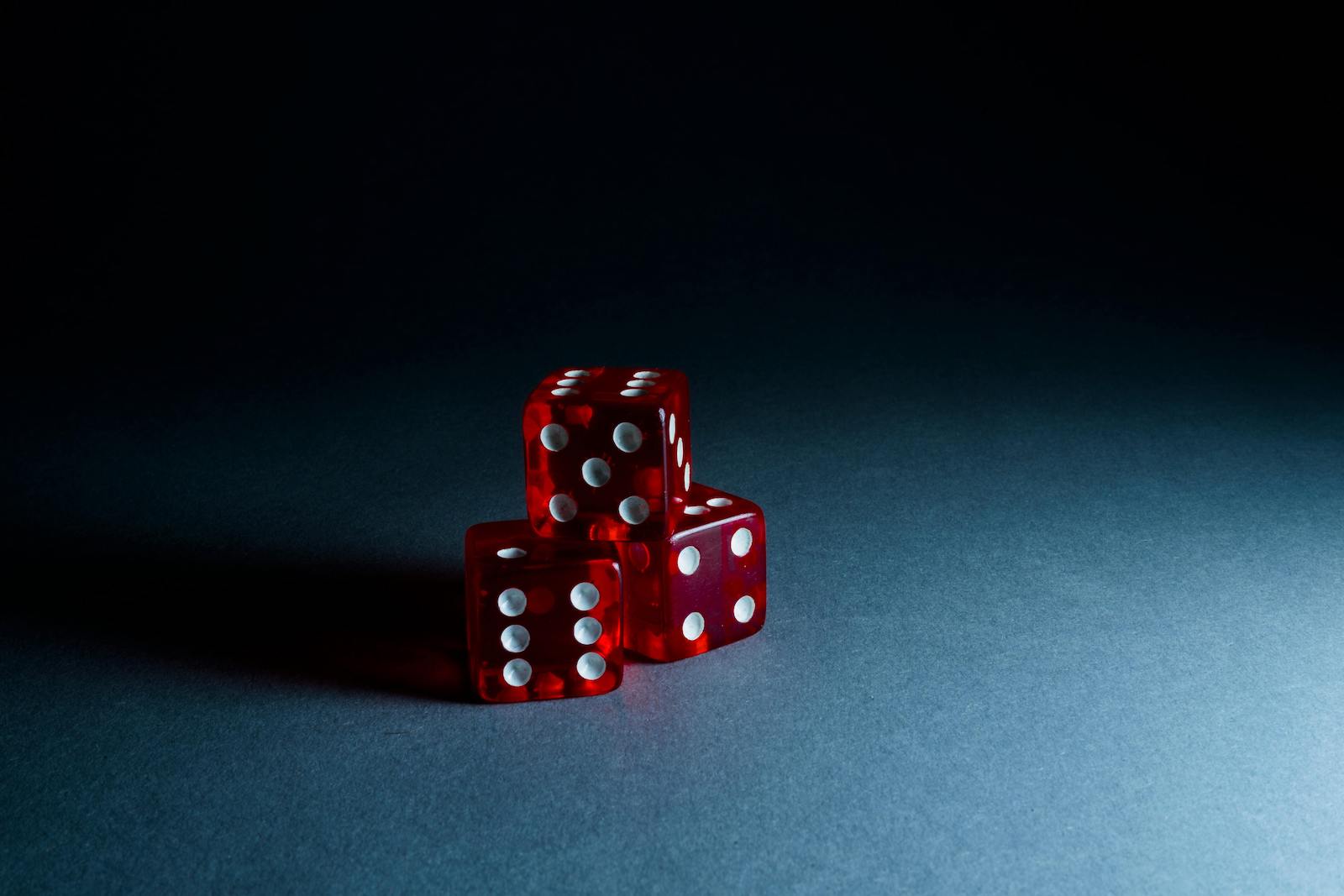 Three translucent red dice with white pips stacked together on a dark blue gradient background