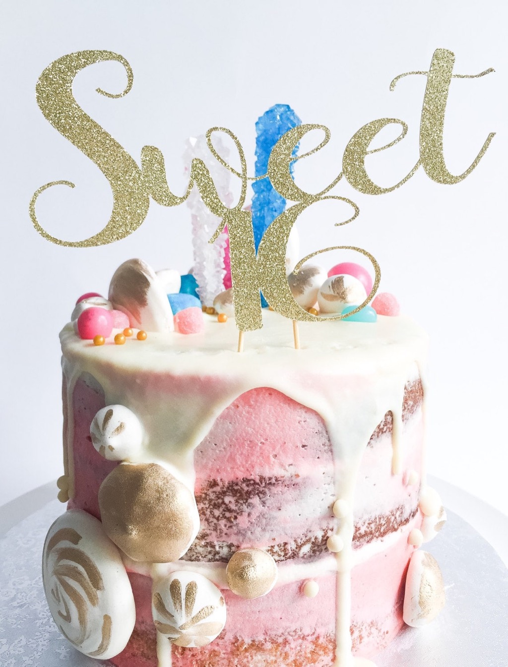 A gold glitter Sweet 16 cake topper on a pink drip cake