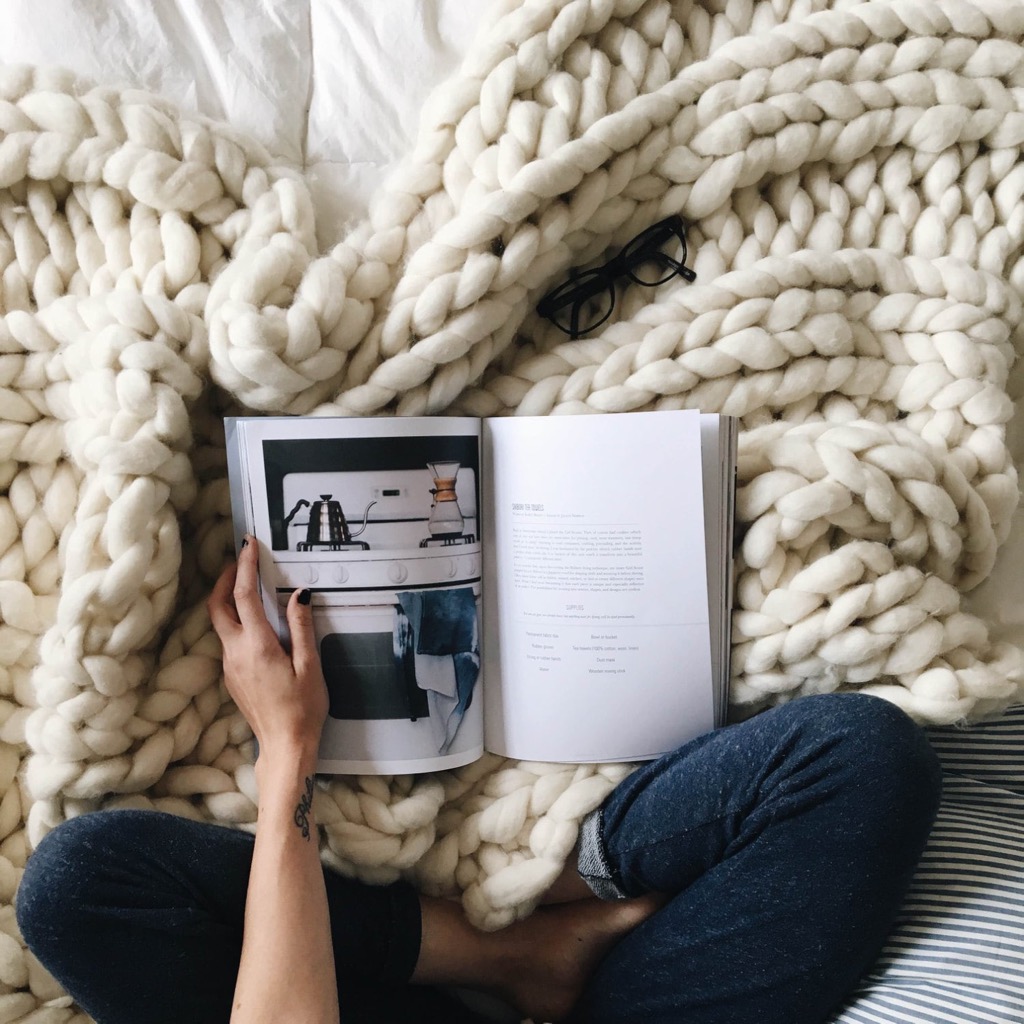 A cozy chunky knit blanket next to an open book
